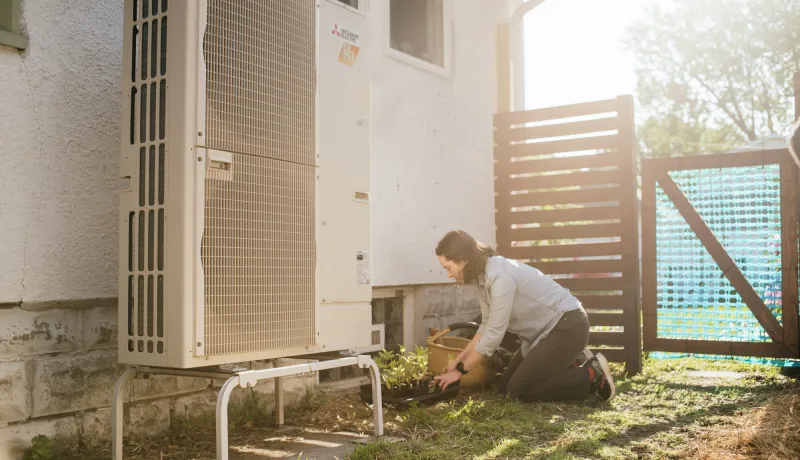A person outside next to their heat pump.
