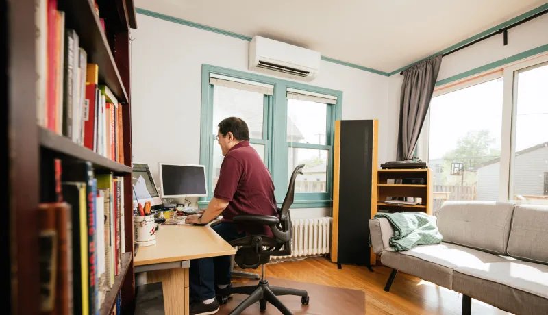 A person sits at their desk with a mini-split system behind them.