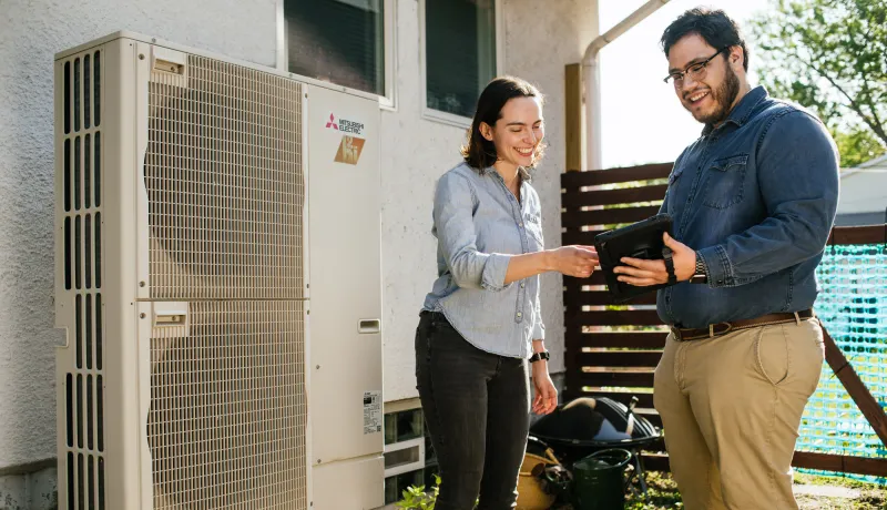 two people looking at information outside on an iPad next to an air source heat pump