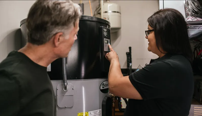 A homeowner stands next to a technician as she points out something on the homeowner's heat pump water heater.