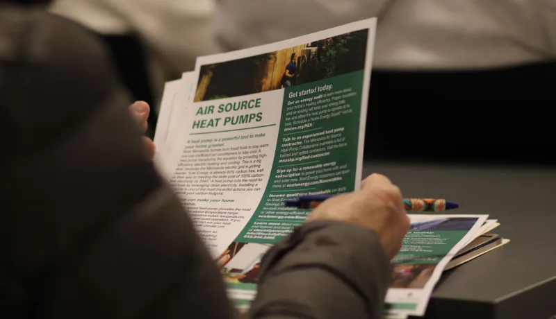 A person holds an informational flyer on air source heat pumps while holding a pen.