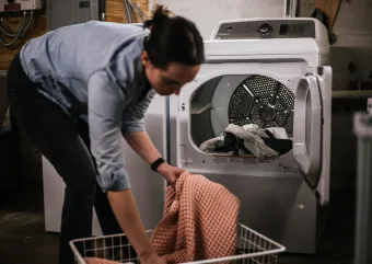 A person stands loading their electric clothes dryer.