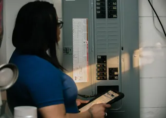 A person stands at an electric panel, inspecting it.