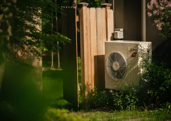 A heat pump stands in the yard of an electrified home.
