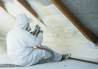 A person in protective gear adds insulation to an attic.