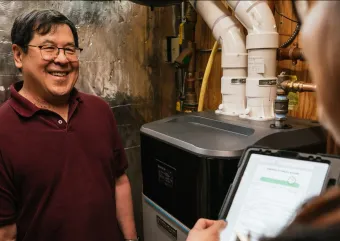 A homeowner stands proudly in front of his heat pump backup system, a boiler.