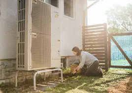 A person outside next to their heat pump.