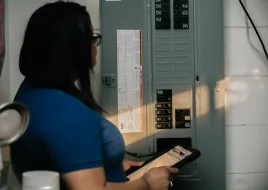 A person stands at an electric panel, inspecting it.
