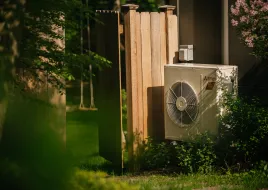 A heat pump stands in the yard of an electrified home.