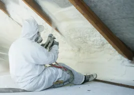 A person in protective gear adds insulation to an attic.