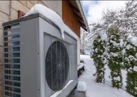 An air source heat pump is installed alongside a home in snowy weather.